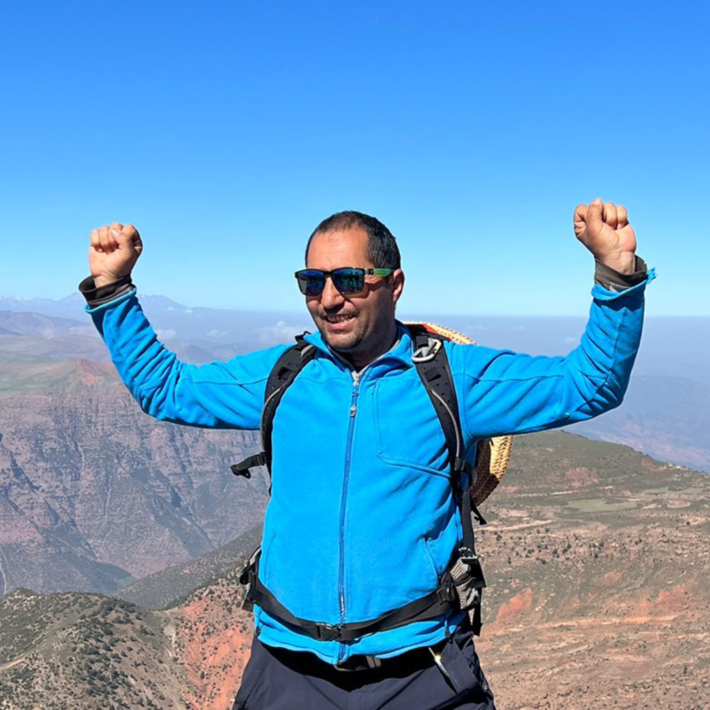 man dressed in blue sport jacket with arms in the air and sunglasses