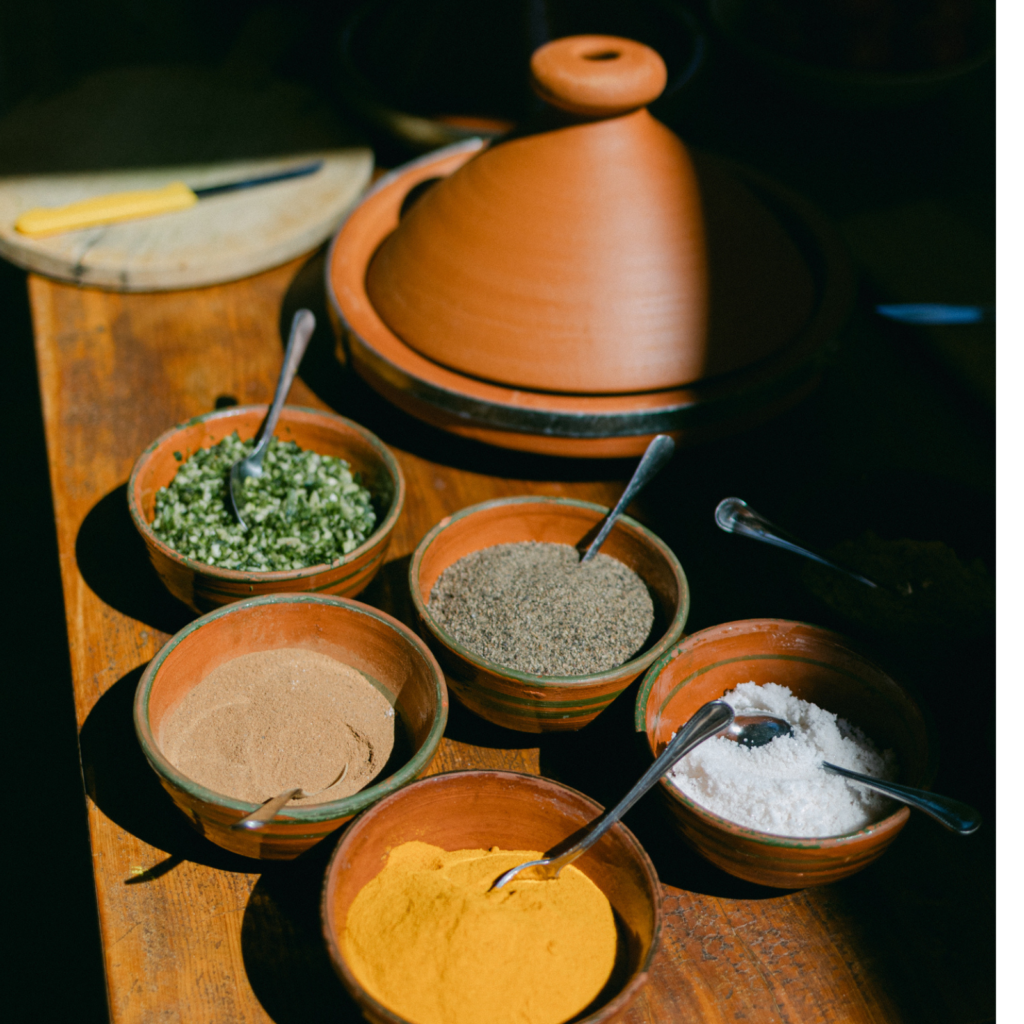 colorful spices and ingredients in small bowls in the sun and a moroccan cooking pot for tangine