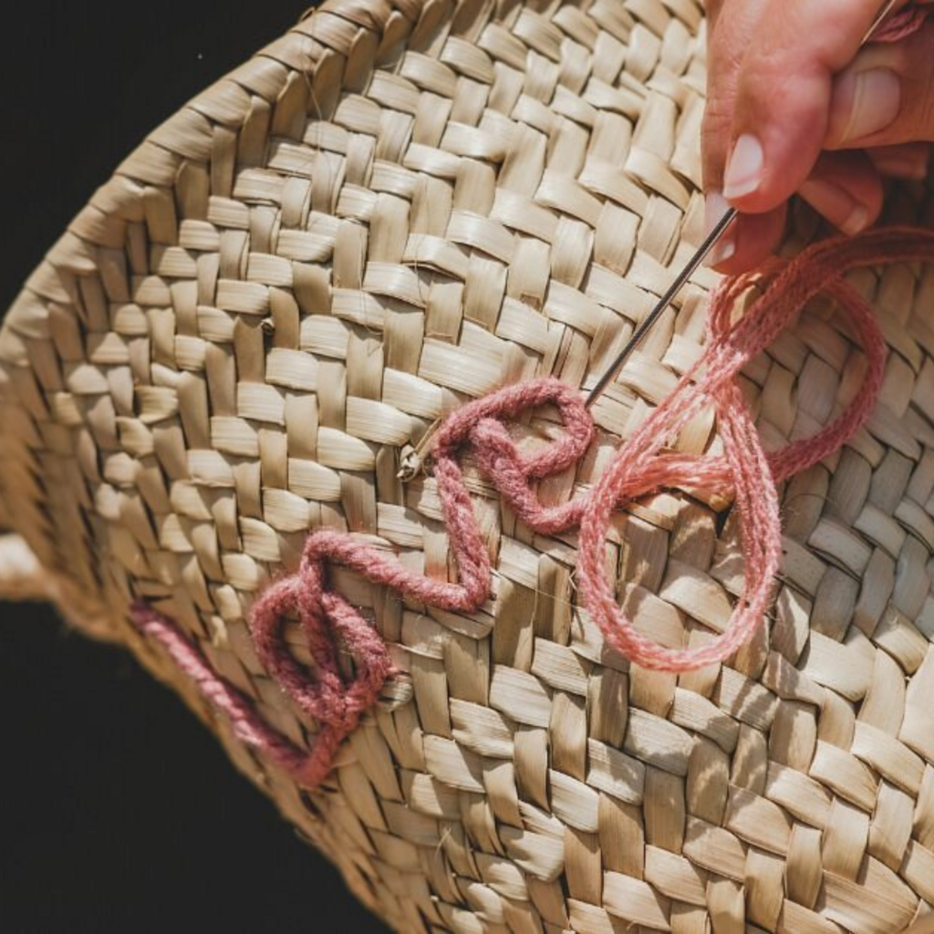 pink embroidery with word love in a basket. hand with needle