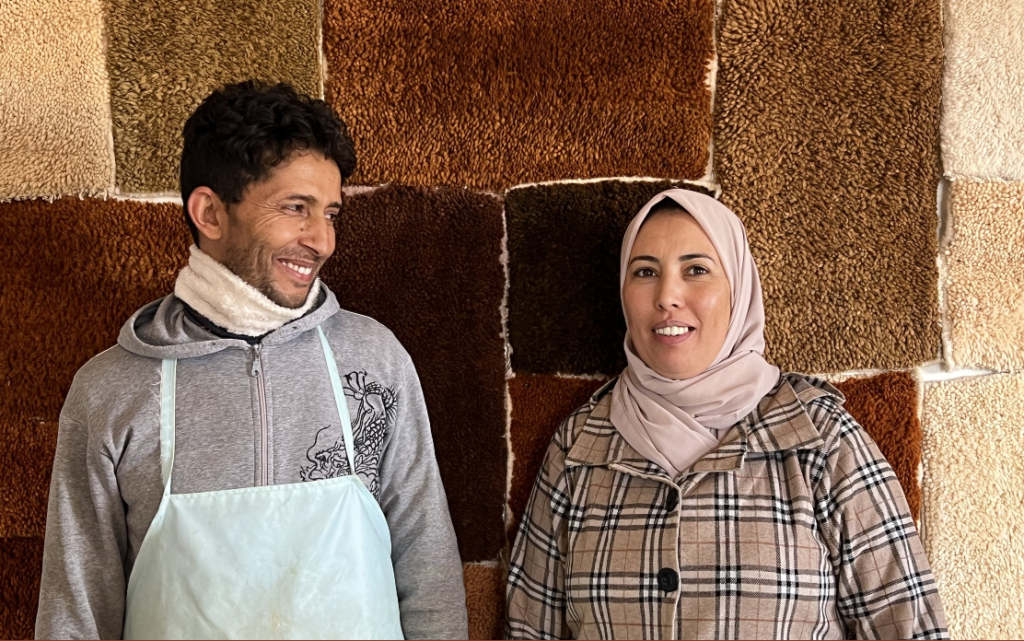 a men and a woman smiling in winter clothing against a rug-covered wall