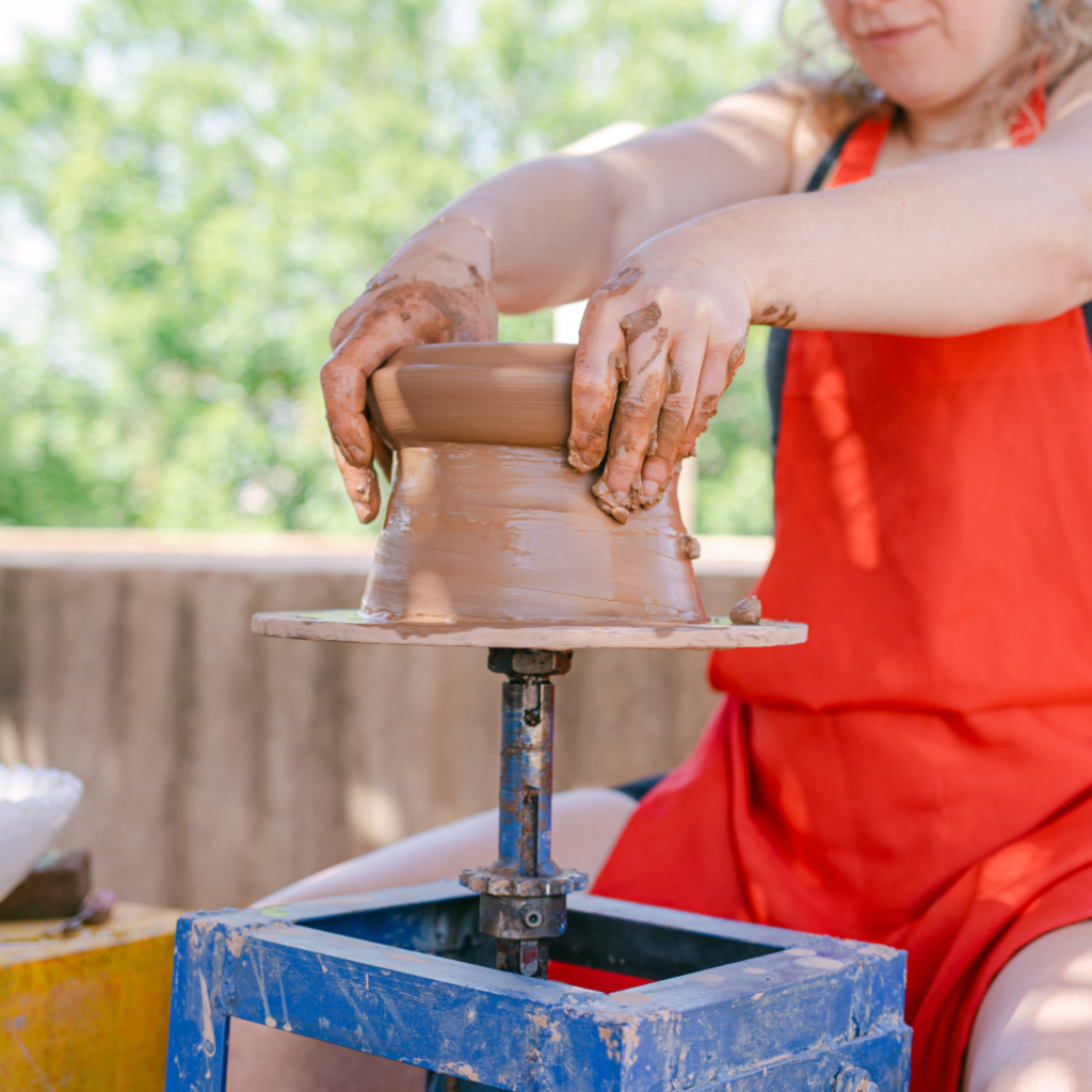 woman doing pottery on a spinning blue wheel