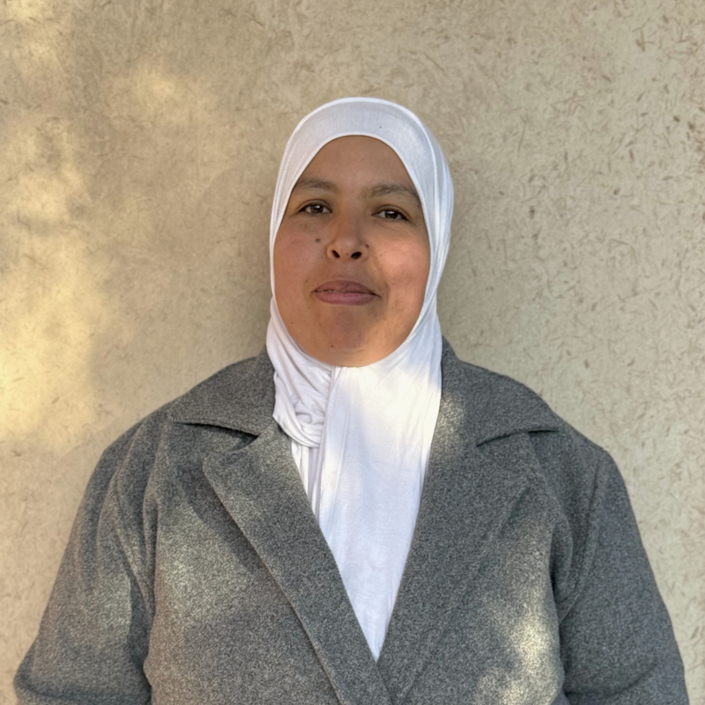 woman wearing a white hijab and grey winter jacket against a beige wall